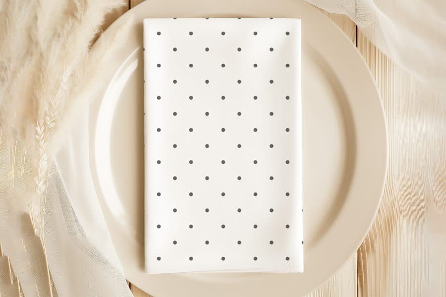 A White Napkin With Dark Gray Polka Dots On A Beige Plate.