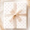 A White Gift Box With Pink Polka Dots And A Beige Ribbon Tied In A Bow.
