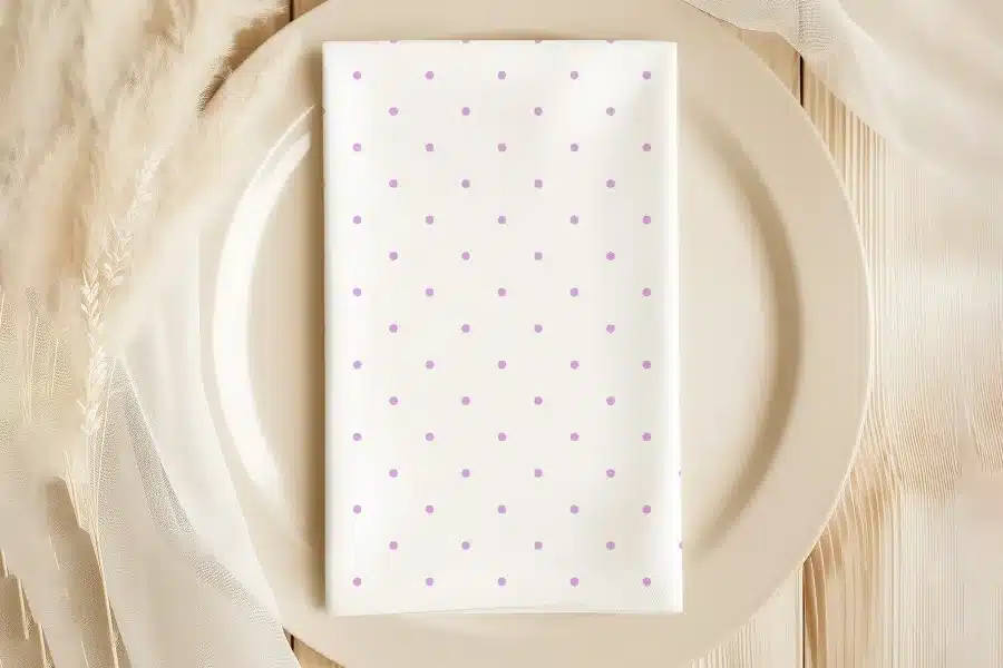 A White Napkin With Light Purple Polka Dots Sits On A Beige Plate.