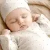 Sleeping Baby Wearing A White Polka Dot Onesie And Matching Hat.