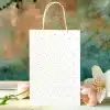 White Polka Dot Gift Bag With Pink Flower And White Lily Next To It.