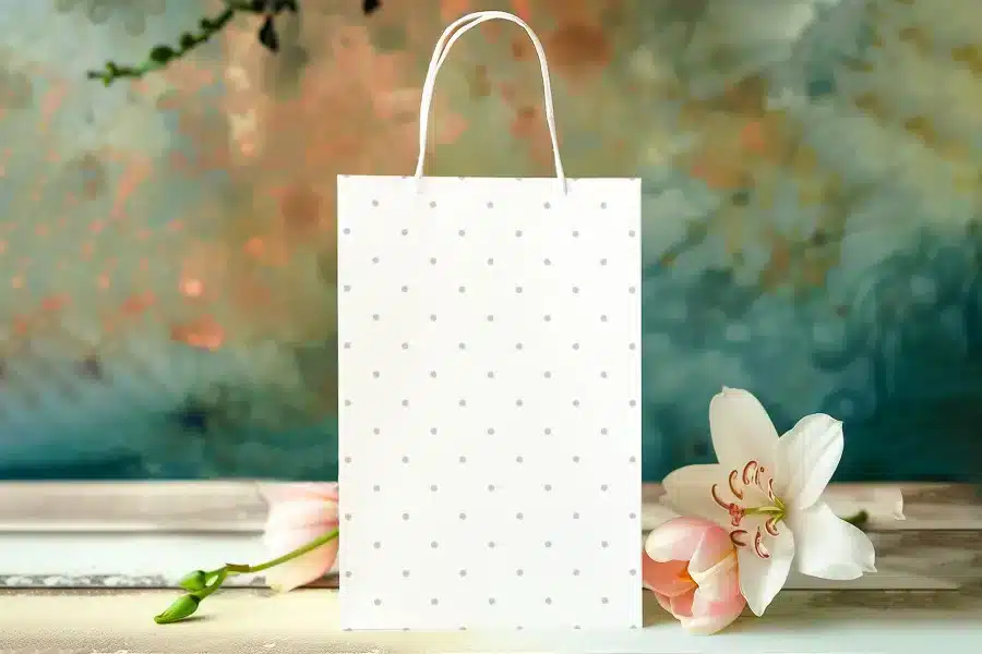 White Polka Dot Gift Bag With Pink Flower And White Lily Next To It.