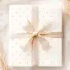 A White Gift Box With Small Gray Dots And A Beige Ribbon Tied In A Bow.