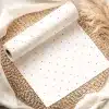 A Roll Of White Wrapping Paper With Light Pink Polka Dots, Partially Unrolled On A Woven Placemat.