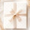 A White Gift Box With Light Beige Polka Dots And A Matching Ribbon Tied In A Bow.