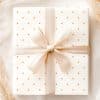 A Cream-Colored Gift Box With Small Orange Dots And A Beige Ribbon Tied In A Bow.
