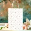White Gift Bag With Red Polka Dots, Next To Pink Flowers.