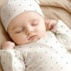 Sleeping Baby Wearing A White, Teal-Polka-Dotted Onesie And Matching Hat.