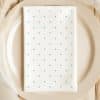 White Dinner Napkin With Light Teal Polka Dots On A Beige Plate.