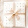 A Gift Box With A Light Beige Ribbon And Light Teal Polka Dots On A White Background.