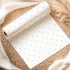 Roll Of White Paper With Light Teal Polka Dots Unfurling On A Woven Mat.