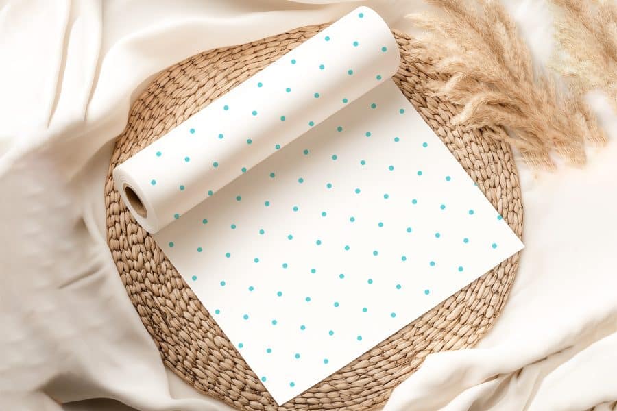 Roll Of White Paper With Light Teal Polka Dots Unfurling On A Woven Mat.