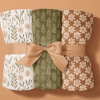 Three Rolled-Up Blankets With Floral And Leaf Patterns, Tied Together With A Beige Ribbon.