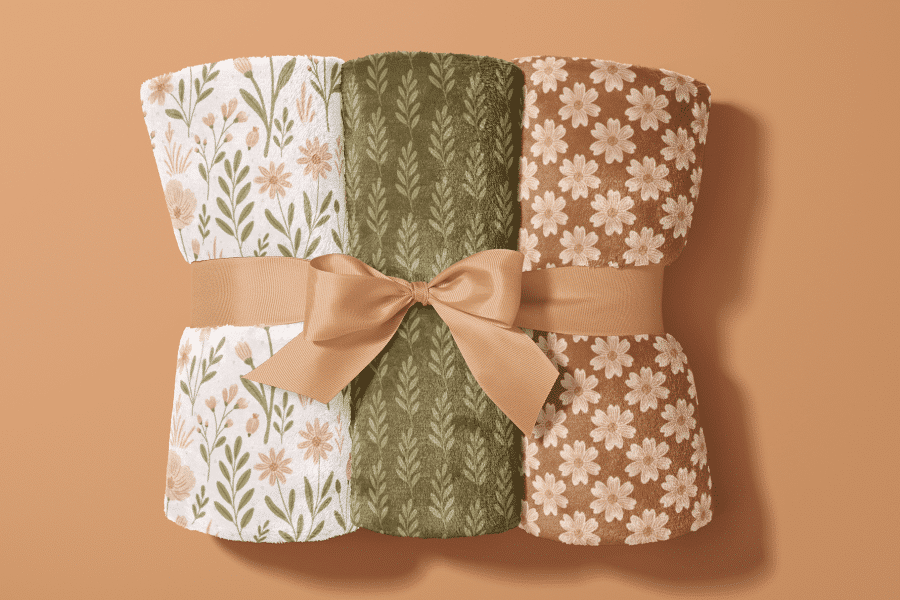 Three Rolled-Up Blankets With Floral And Leaf Patterns, Tied Together With A Beige Ribbon.