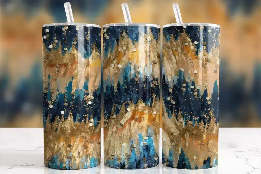 Three tall tumblers with gold, blue, and beige abstract designs and clear straws.