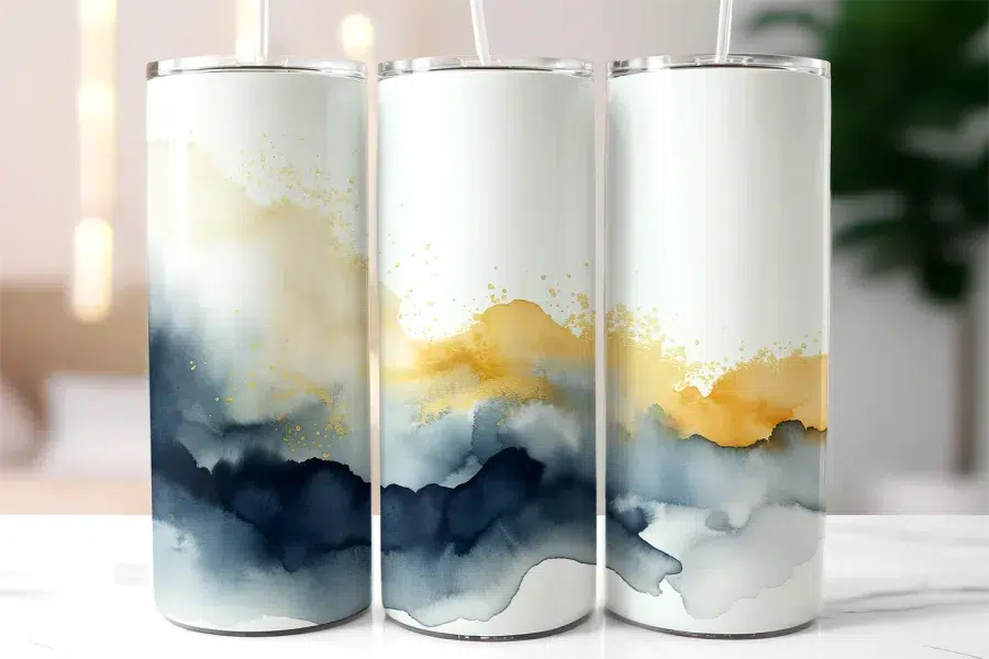 Three Tall Tumblers With Abstract Watercolor Designs In Shades Of Blue, Gold, And White.