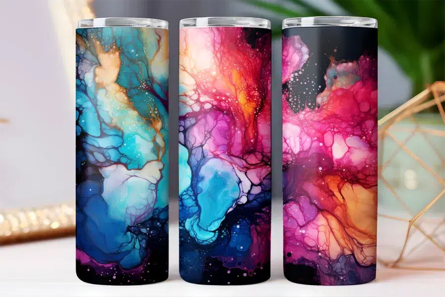 Three tall tumblers with abstract alcohol ink designs in shades of blue, pink, and purple.