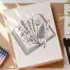 Line Drawing Of Flowers And A Fern Emerging From An Open Book, With A Pen Resting On Top.