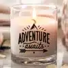 A Lit Candle In A Clear Glass Jar With The Words Adventure Awaits Printed On The Side.