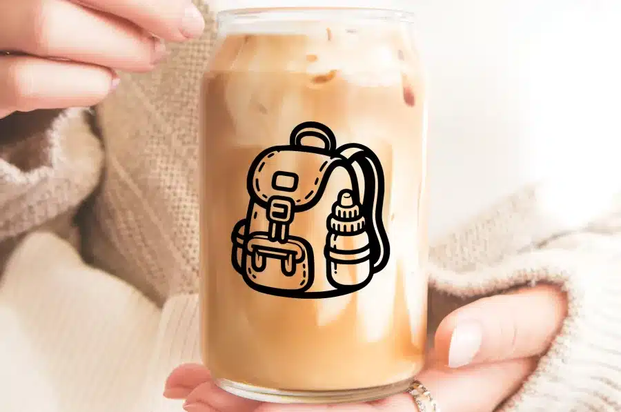 Hands Holding A Glass Of Iced Coffee With A Backpack And Water Bottle Design.