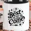 White Coffee Mug With A Black Handle, Displaying The Text The Best Is Yet To Come In A Stylized Font With Decorative Elements.