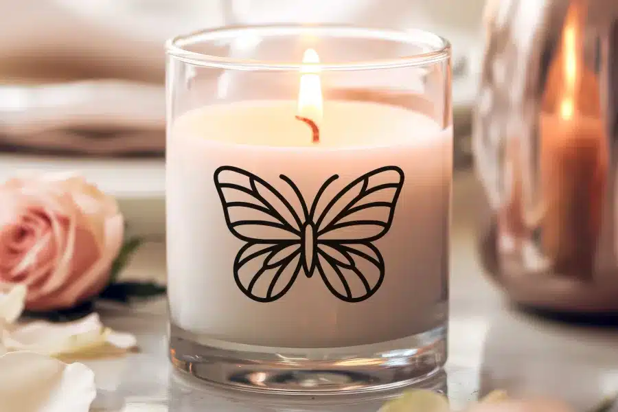 A lit candle in a glass jar decorated with a black butterfly design.