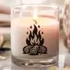 A Lit Candle In A Clear Glass Jar With A Campfire Design On The Side.