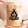 A Person Holds A Glass Iced Coffee With A Campfire Design.