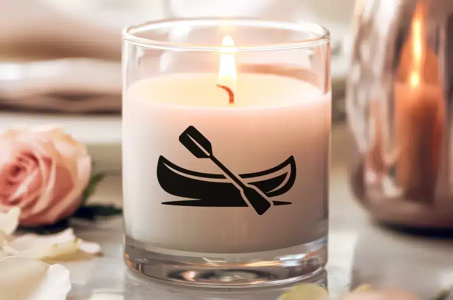 A Lit Candle In A Clear Glass Jar Features A Canoe And Paddle Design.