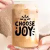 Close-Up Of Hands Holding A Glass Jar Filled With Iced Coffee. The Jar Is Decorated With The Text Choose Joy.