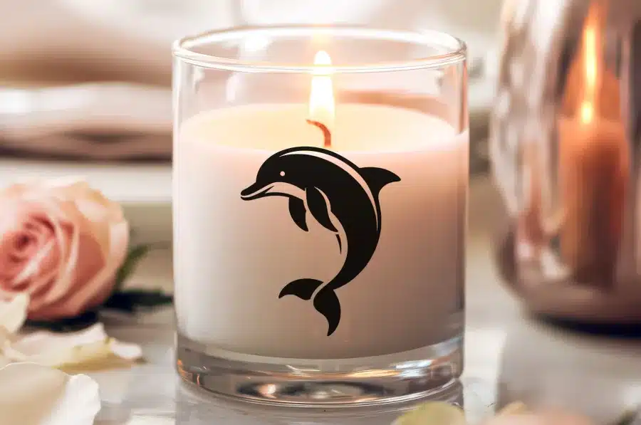 A Lit Candle In A Glass Jar Features A Black Dolphin Design.