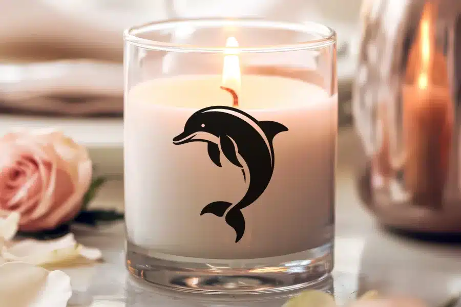 A lit candle in a glass jar features a black dolphin design.