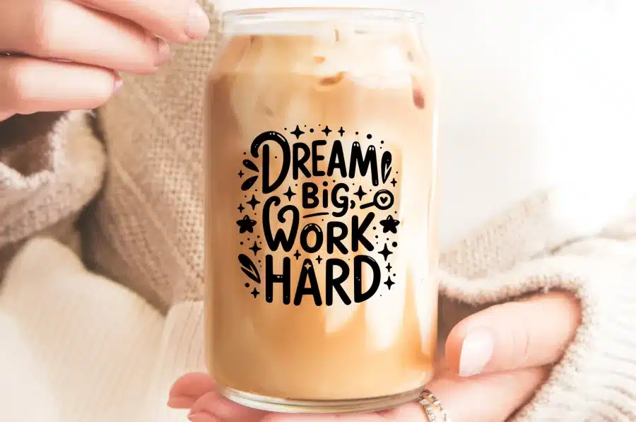 A Person'S Hands Holding A Glass Iced Coffee Can With The Text Dream Big Work Hard.
