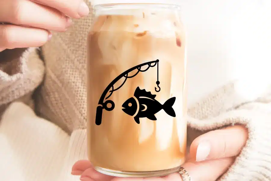 A person holding a glass of iced coffee with a fishing rod and fish design.