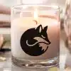 A Lit Candle In A Clear Glass Jar, Featuring A Black Silhouette Of A Curled-Up Fox.
