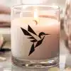 A Lit Candle In A Clear Glass Jar, Featuring A Geometric Hummingbird Design.