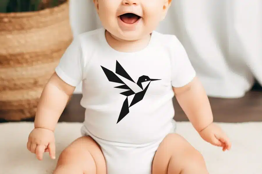 A Smiling Baby Wearing A White Onesie With A Geometric Hummingbird Design.