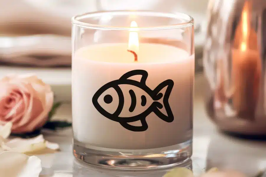 A Lit Candle In A Glass Jar With A Black Fish Illustration On The Side.