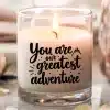 A Lit Candle In A Clear Glass Jar With The Text You Are Our Greatest Adventure.