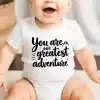 Baby Wearing A White Onesie That Says You Are Our Greatest Adventure.