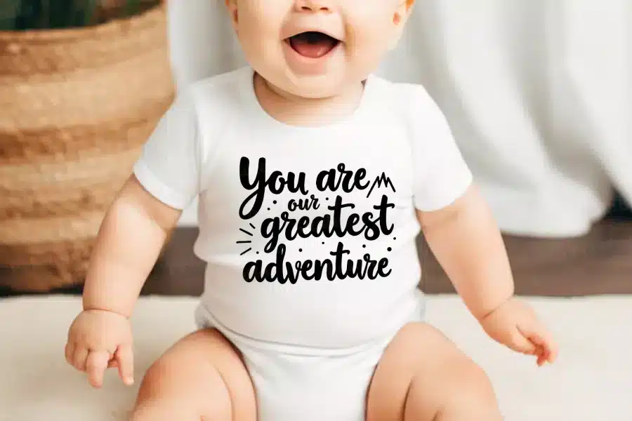 Baby wearing a white onesie that says You are our greatest adventure.