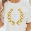 Woman Wearing A White T-Shirt With A Gold Laurel Wreath Design.