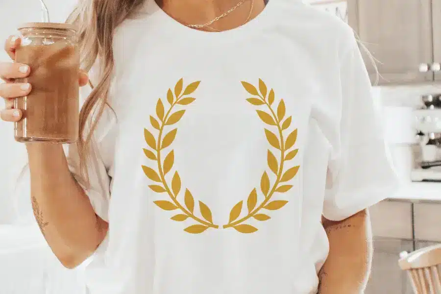Woman Wearing A White T-Shirt With A Gold Laurel Wreath Design.
