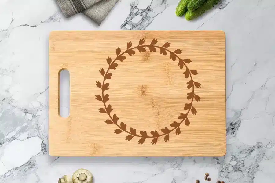 Light Brown Bamboo Cutting Board With A Dark Brown Engraved Wreath Design.
