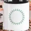 White Coffee Mug With A Black Handle, Featuring A Sage Green Leafy Wreath Design.