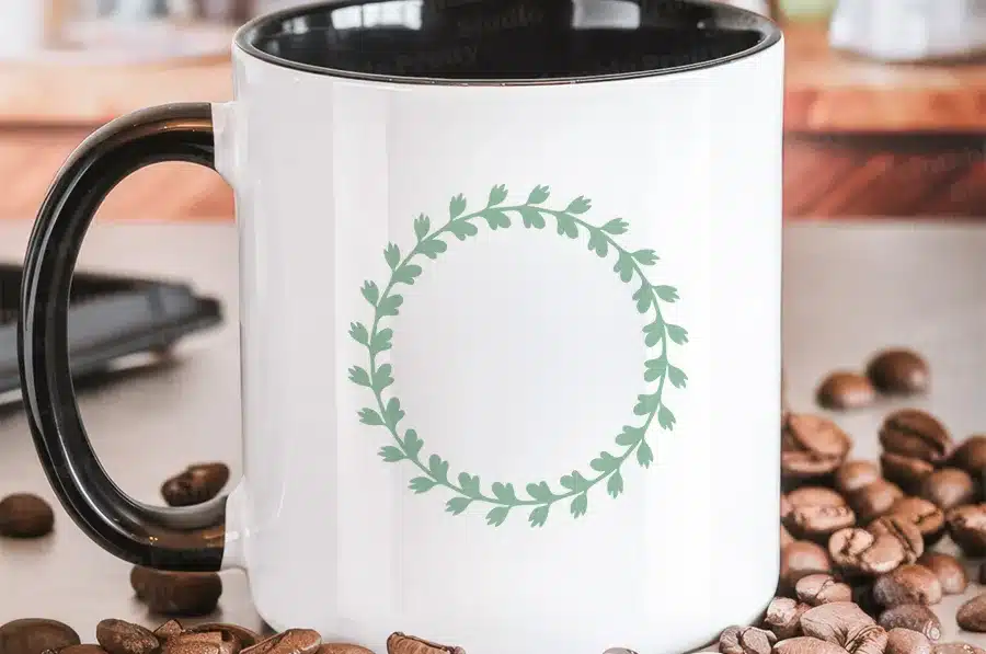 White Coffee Mug With A Black Handle, Featuring A Sage Green Leafy Wreath Design.