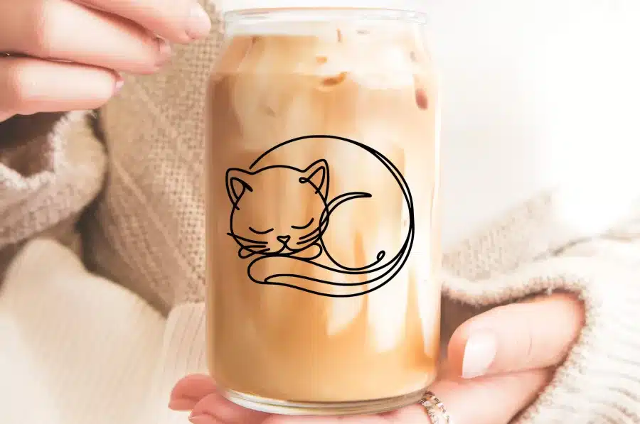 A Glass Of Iced Coffee Featuring A Line Drawing Of A Sleeping Cat.