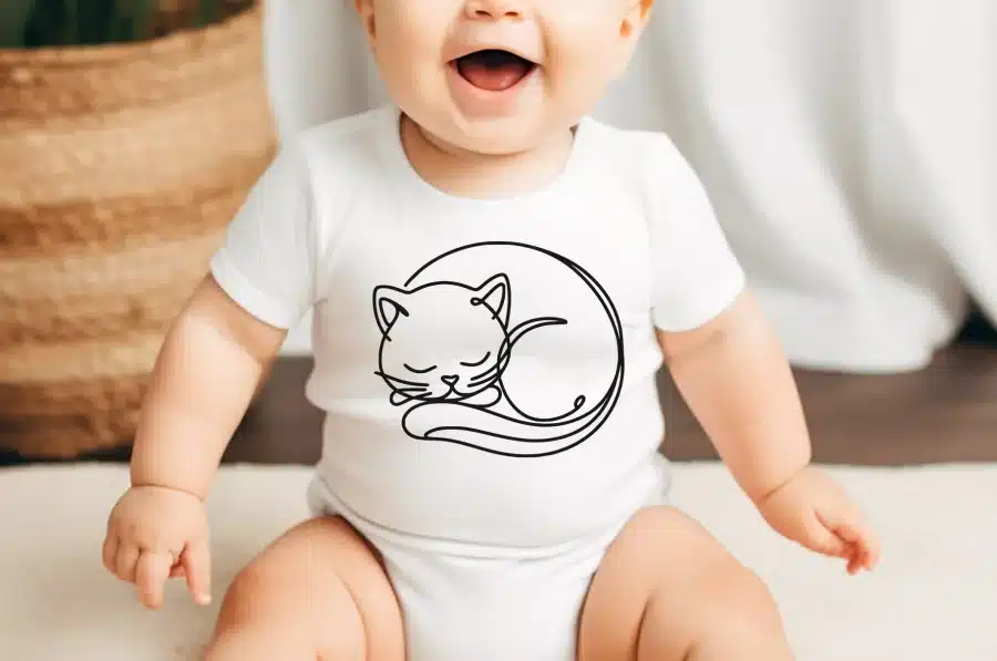 Baby Wearing A White Onesie With A Line Drawing Of A Sleeping Cat.