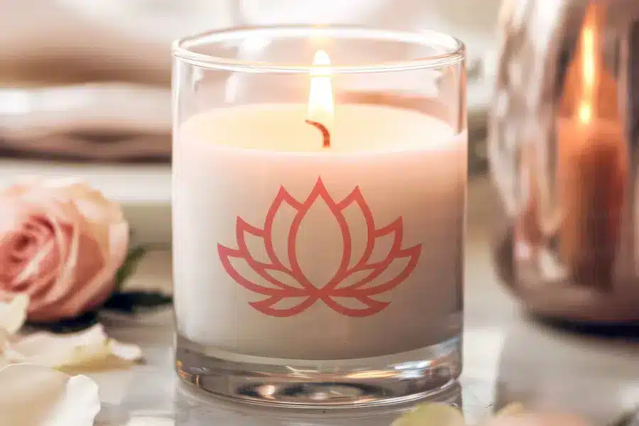 A lit candle in a glass jar with a lotus flower design.