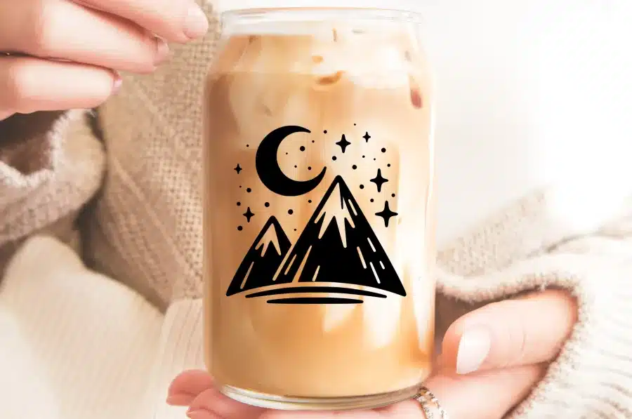 A Glass Of Iced Coffee With A Mountain And Moon Design.